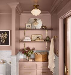 a bathroom with pink walls and shelving above the toilet is decorated in gold accents