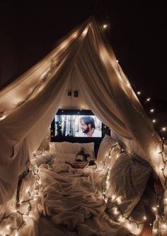 a bed covered in white sheets and lights under a tv screen that is turned on