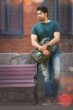 a man sitting on top of a bench next to a brick wall and holding a bag