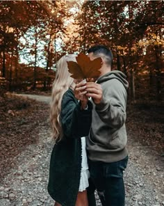 a man and woman holding up a leaf in the middle of a road with trees behind them