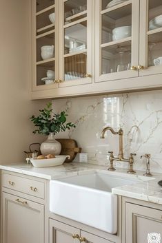 a kitchen with white cabinets and marble counter tops, gold pulls on the cupboards