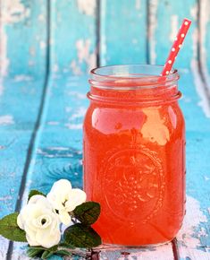 a mason jar with a straw and some flowers on the side, sitting on a blue wooden table