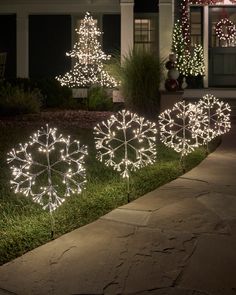 lighted snowflakes in front of a house at night with christmas lights on the trees