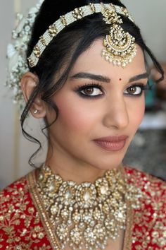 a woman in a red and gold bridal outfit with jewelry on her head, looking at the camera