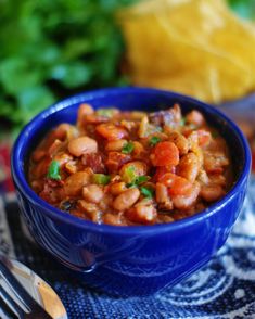 a blue bowl filled with beans and vegetables on top of a table next to a fork