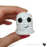 a hand holding a small white crocheted object with a smiley face on it