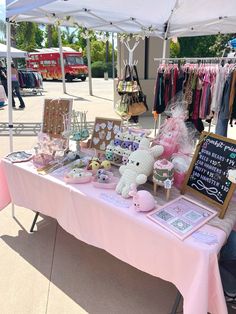 a pink table topped with lots of stuffed animals next to a white tent covered in clothes