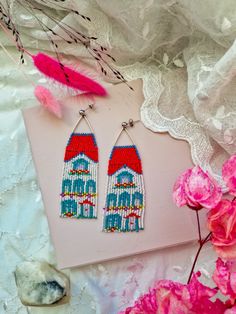 the beaded earrings are on display next to pink flowers and white doily with feathers