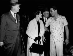 an old black and white photo of three men talking to one another while the other man is wearing a hat