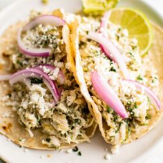 two fish tacos with onions and cilantro on a white plate next to lime wedges