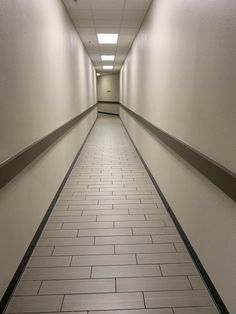 a long hallway with white walls and tile flooring on both sides, leading to an exit door