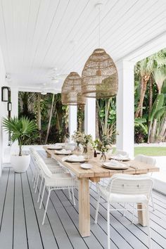 an outdoor dining area with white wicker chairs and wooden table