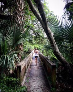 a woman walking across a bridge surrounded by trees