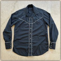 For your consideration Original vintage 1970s era black men's Pearl Snap western Shirt White piping Long sleeve Cotton blend Made in USA Long tails Form Fit Interior collar straighteners Button front Three button cuffs Looks handmade (check photos for interior) .. in gently used condition .. no holes or tears or noticeable soiling .. no neckline closure Shown on men's vintage size large mannequin torso Measures approximately 23.5" pit to pit (47" chest) 31" top neckline to bottom 19.25" across s Retro Black Tops With Buttons, Black Retro Tops With Buttons, Black Retro Top With Buttons, Retro Black Button-up Shirt, Vintage Black Buttoned Tops, Retro Black Collared Shirt, Vintage Black Tops With Buttons, Western Black Button-up Shirt, Western Style Black Button-up Shirt