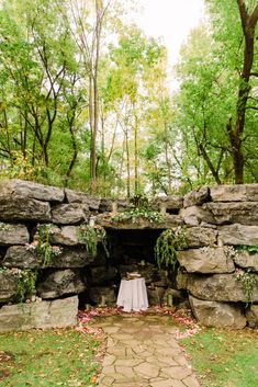 a table set up in the middle of a stone wall with greenery and flowers