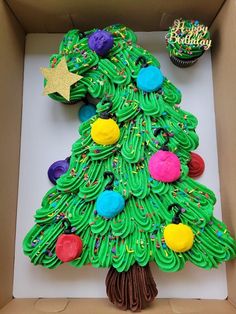 a cupcake decorated like a christmas tree in a box with decorations on the top