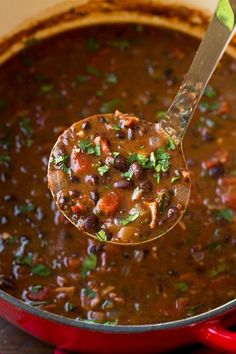 a ladle full of chili and beans in a red pot