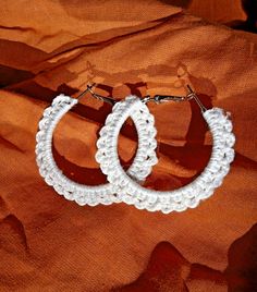 two white crocheted hoop earrings sitting on top of an orange fabric covered surface