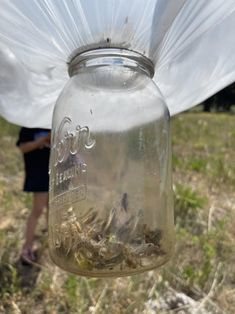 a mason jar filled with lots of dirt sitting on top of a grass covered field