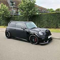 a black minivan parked in front of a house on the street next to a hedge