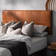 a bed with many pillows on it and a brown headboard in the corner next to a lamp