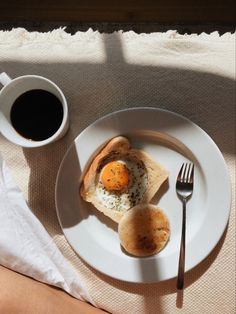 an egg and some bread on a plate next to a cup of coffee