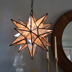 a star shaped light hanging from the ceiling next to a mirror and candle holder on a table