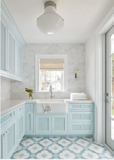 a blue and white bathroom with tile flooring, sink, cabinets and window in the corner