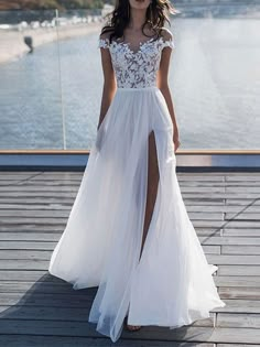 a woman in a white dress is standing on a dock with her legs slited