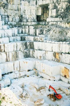 an orange excavator sitting in the middle of a large stone quarry area