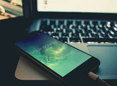 an open laptop computer sitting on top of a wooden desk next to a cell phone