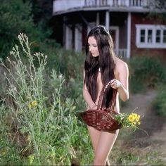 a woman with long dark hair is holding a basket and flowers in front of her