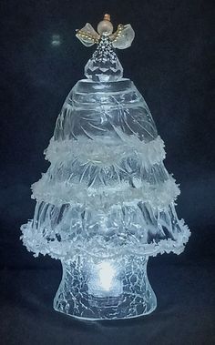 a clear glass christmas tree with angel wings on it's top and lights in the bottom