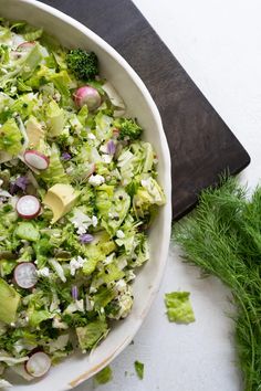 a white bowl filled with broccoli and radishes on top of a wooden cutting board