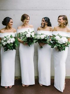 four bridesmaids in white dresses holding bouquets and smiling at each other while standing against a wall