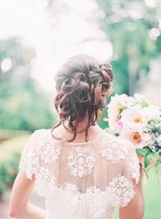 the back of a woman's head with flowers in her hair, holding a bouquet