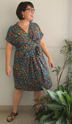 a woman standing next to a potted plant wearing glasses and a dress with colorful shapes on it