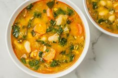 two white bowls filled with vegetable soup on top of a marble counter next to a spoon