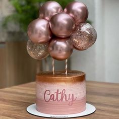 there is a cake with pink and gold balloons on it that says cathy in the center