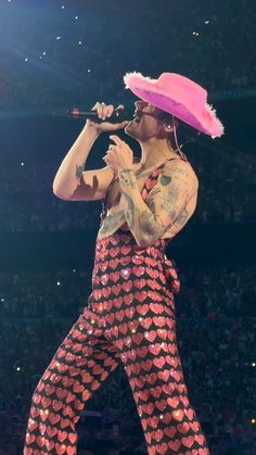 a man in pink hat and pants on stage holding a microphone with his right hand