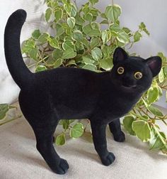 a black cat figurine standing next to a plant