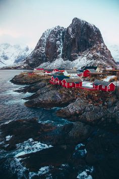 a red house sitting on top of a rocky cliff next to the ocean with snow covered mountains in the background