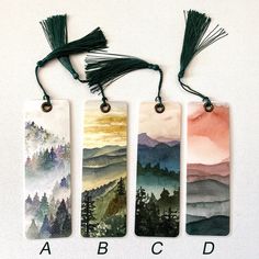 three bookmarks with mountains and trees painted on them are hanging from strings that have tassels