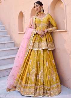 a woman standing in front of a wall wearing a yellow and pink lehenga