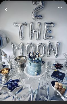 a table topped with a blue cake and lots of silver balloons that spell out the word's the moon