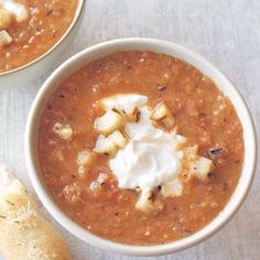 two bowls filled with soup next to a piece of bread on top of a table