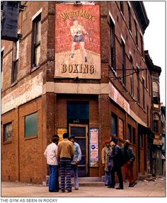 several people are standing in front of a brick building with a boxing sign on it