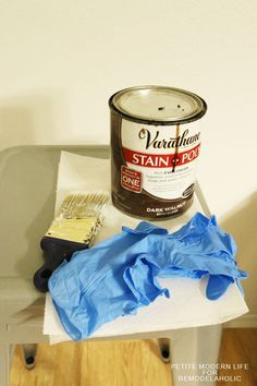 a can of paint sitting on top of a chair next to a blue cloth and brush