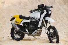 a yellow and white dirt bike parked in the sand