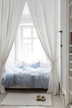 a bedroom with a bed, bookshelf and white curtains over it's windows